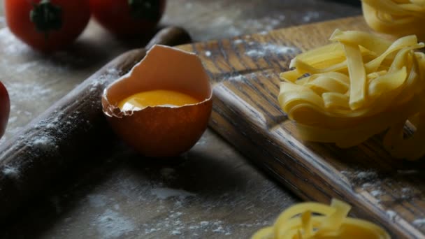 生の小麦粉製品は、ビューを閉じます.イタリア料理。壊れた卵黄、素朴なスタイルのチェリートマトの横にある木製のキッチンボード上のタグリアテルやフェットチーネパスタ巣. — ストック動画