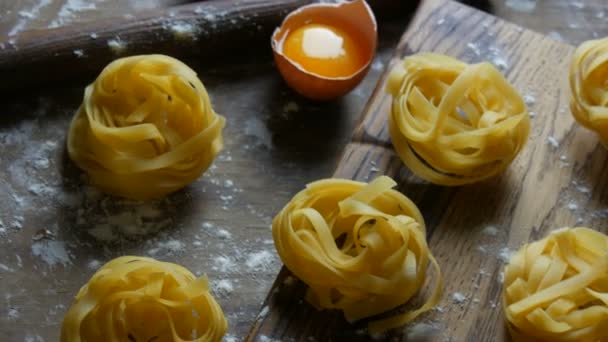 Fila di cibo nazionale italiano. Prodotti di farina cruda vista da vicino. Tagliatelle o fettuccine nidificano su una tavola da cucina in legno accanto ad un tuorlo d'uovo rotto in stile rustico . — Video Stock