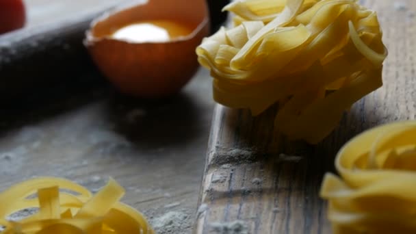 Raw flour products close up view. National italian food. Tagliatelle or fettuccine pastas nests on a wooden kitchen board next to a broken egg yolk, cherry tomatoes in a rustic style. — Stock Video