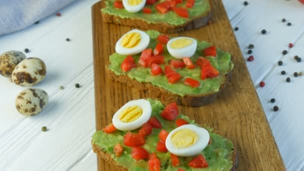 Comida vegana saludable. Untar el puré de aguacate sobre un pan tostado. Preparando sabrosas tostadas de aguacate para el desayuno. Cocinar bruschetta con tomates cherry y huevos de codorniz . — Vídeo de stock