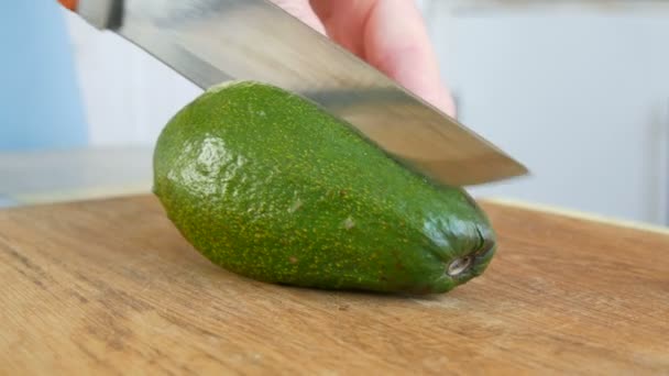 Wytnij awokado na drewnianej tablicy kuchennej dużym nożem. Vegan Zdrowe jedzenie z bliska widok — Wideo stockowe