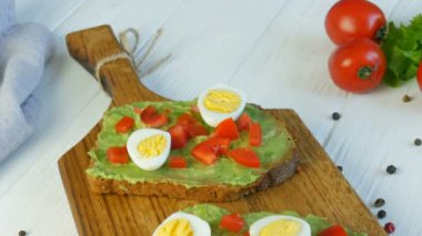 Sağlıklı vejetaryen yemeği. Kavrulmuş kahverengi ekmeğin üzerine avakado ezmesi dök. Kahvaltıda lezzetli avokado tostu yapıyorum. Kiraz domatesli bruschetta ve bıldırcın yumurtası pişiriyorum..