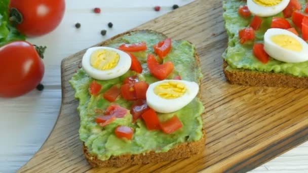 Healthy Vegan food. Spread mashed avocado on a toasted brown bread. Making tasty avocado toast for breakfast. Cooking bruschetta with cherry tomatoes and quail eggs. — Stock Video