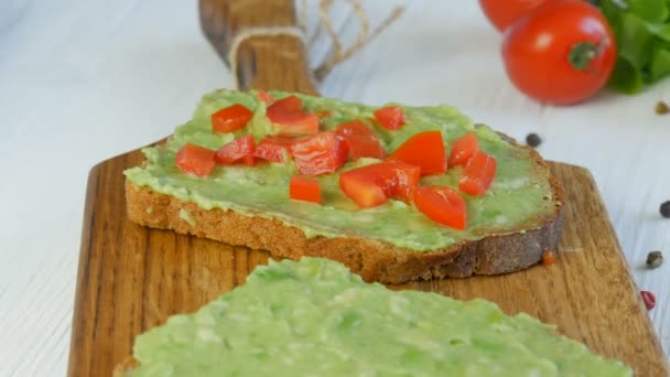 Kavrulmuş kahverengi ekmeğin üzerine avakado ezmesi dök. Kahvaltıda lezzetli avokado tostu yapıyorum. Kiraz domatesli bruschetta ve bıldırcın yumurtası pişirmek. Sağlıklı vejetaryen yemekleri — Stok video