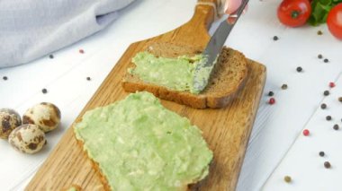 Kızarmış ekmeğin üzerine bıçakla ezilmiş avokado. Kahvaltıda lezzetli avokado tostu yapıyorum. Kiraz domatesli bruschetta ve bıldırcın yumurtası pişirmek. Yakından bak. Sağlıklı vejetaryen yemekleri