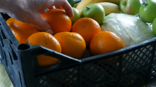Kadın eli mandalina ve elma alır. Meyve ve sebzeli kutu yakın. Coronavirus salgını ve sosyalleşme sırasında yiyecek dağıtım hizmetleri. İnternetten alışveriş. Yemek Bağışı — Stok video