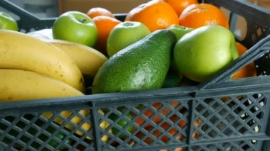 Meyve ve sebzelerle dolu bir kutu muz, mandalina, avokado lahanası. Coronavirus salgını ve sosyalleşme sırasında yiyecek dağıtım hizmetleri. İnternetten alışveriş. Yemek Bağışı