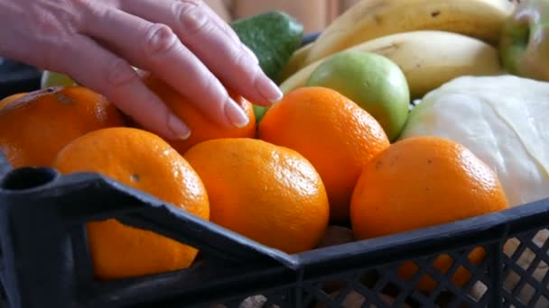 Vrouwelijke hand neemt mandarijn en appel. Doos met groenten en fruit close-up. Levering van voedsel tijdens de pandemie met het coronavirus en op sociale afstand. Online winkelen. Maaltijden Voedseldonaties — Stockvideo