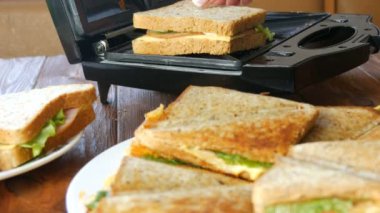 Ev mutfağında sabah kahvaltısı. Pastırmalı sandviç, çedar peyniri ve marul özel bir tost makinesinde ya da sandviç makinesinde kızartılır. Özel mutfak spatulası taze sandviç ekmeği alır.