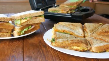Ev mutfağında sabah kahvaltısı. Pastırmalı sandviç, çedar peyniri ve marul özel bir tost makinesinde ya da sandviç makinesinde kızartılır. Özel mutfak spatulası taze sandviç ekmeği alır.