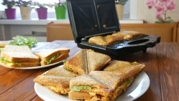 Desayuno por la mañana en la cocina casera. Los sándwiches con tocino, queso cheddar y lechuga se fríen en una tostadora especial o una sándwich. Espátula especial cocina toma pan sándwich fresco — Vídeos de Stock