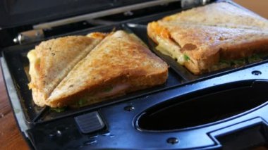 Ev mutfağında sabah kahvaltısı. Pastırmalı sandviç, çedar peyniri ve marul özel bir tost makinesinde ya da sandviç makinesinde kızartılır.