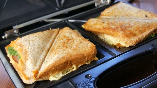 Ochtend ontbijt in de huiskeuken. Sandwiches met spek, cheddar kaas en sla worden gebakken in een speciale broodrooster of een broodjesmaker — Stockvideo