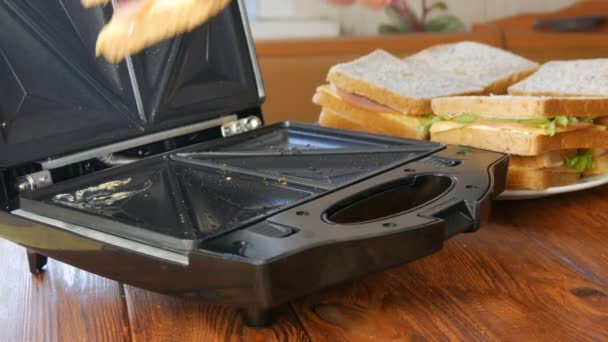 Morning breakfast in the home kitchen. Sandwiches with bacon, cheddar cheese and lettuce are fried in a special toaster or a sandwich maker. Special kitchen spatula takes fresh sandwich bread — Stock Video