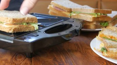 Ev mutfağında sabah kahvaltısı. Pastırmalı sandviç, çedar peyniri ve marul özel bir tost makinesinde ya da sandviç makinesinde kızartılır. Özel mutfak spatulası taze sandviç ekmeği alır.