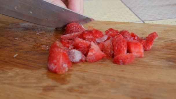 Γυναικεία χέρια κόβουν μια παγωμένη φράουλα με ένα μαχαίρι για μελλοντική φρουτοσαλάτα ή smoothie σε ξύλινο πίνακα κουζίνας. Πρωινό στο σπίτι — Αρχείο Βίντεο