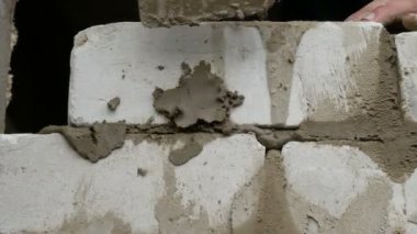 Bir inşaatçının erkek eli taze ıslak çimentoya tuğla döşedi. İnşaat alanındaki bir sıra beyaz tuğla. Yakın görüş alanında. Duvar