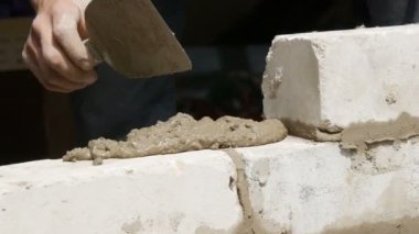 Bir inşaatçının erkek eli taze ıslak çimentoya tuğla döşedi. İnşaat alanındaki bir sıra beyaz tuğla. Yakın görüş alanında. Duvar