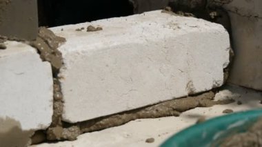 Bir inşaatçının erkek eli taze ıslak çimentoya tuğla döşedi. İnşaat alanındaki bir sıra beyaz tuğla. Yakın görüş alanında. Duvar