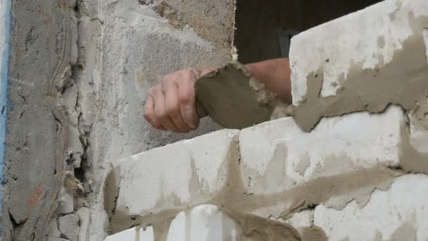 Male hands of a builder lay a brick on fresh wet cement. A row of white brick at a construction site close up view. Wall — Stock Video