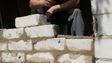 Bir inşaatçının erkek eli taze ıslak çimentoya tuğla döşedi. İnşaat alanındaki bir sıra beyaz tuğla. Yakın görüş alanında. Duvar
