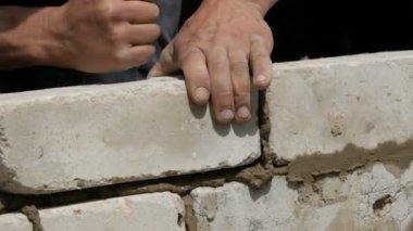 Bir inşaatçının erkek eli taze ıslak çimentoya tuğla döşedi. İnşaat alanındaki bir sıra beyaz tuğla. Yakın görüş alanında. Duvar