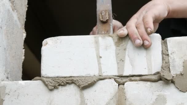 Las manos masculinas del constructor ponen el ladrillo sobre el cemento fresco mojado. Una fila de ladrillos blancos en un sitio de construcción vista de cerca. Pared — Vídeos de Stock