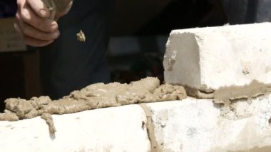 Bir inşaatçının erkek eli taze ıslak çimentoya tuğla döşedi. İnşaat alanındaki bir sıra beyaz tuğla. Yakın görüş alanında. Duvar