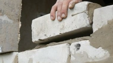 Bir inşaatçının erkek eli taze ıslak çimentoya tuğla döşedi. İnşaat alanındaki bir sıra beyaz tuğla. Yakın görüş alanında. Duvar