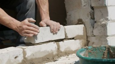 Bir inşaatçının erkek eli taze ıslak çimentoya tuğla döşedi. İnşaat alanındaki bir sıra beyaz tuğla. Yakın görüş alanında. Duvar