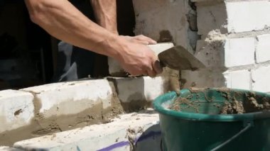 Bir inşaatçının erkek eli taze ıslak çimentoya tuğla döşedi. İnşaat alanındaki bir sıra beyaz tuğla. Yakın görüş alanında. Duvar