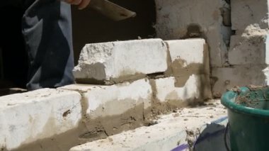 Bir inşaatçının erkek eli taze ıslak çimentoya tuğla döşedi. İnşaat alanındaki bir sıra beyaz tuğla. Yakın görüş alanında. Duvar