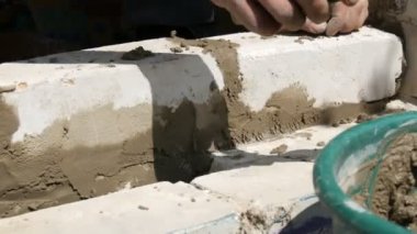 Bir inşaatçının erkek eli taze ıslak çimentoya tuğla döşedi. İnşaat alanındaki bir sıra beyaz tuğla. Yakın görüş alanında. Duvar