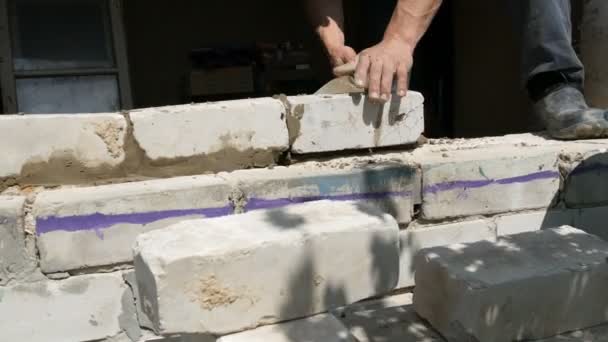 Egy építész férfi keze egy téglát fektet friss nedves betonra. Egy sor fehér tégla egy építkezésen, közelről. Fal — Stock videók