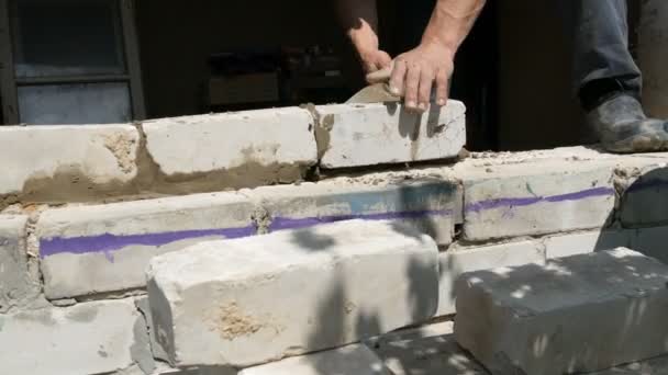 Male hands of a builder lay a brick on fresh wet cement. A row of white brick at a construction site close up view. Wall — Stock Video