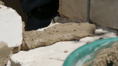 Bir inşaatçının erkek eli taze ıslak çimentoya tuğla döşedi. İnşaat alanındaki bir sıra beyaz tuğla. Yakın görüş alanında. Duvar