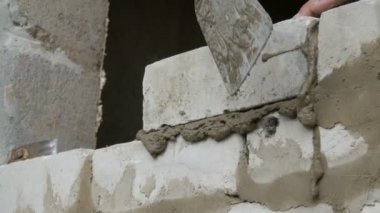 Bir inşaatçının erkek eli taze ıslak çimentoya tuğla döşedi. İnşaat alanındaki bir sıra beyaz tuğla. Yakın görüş alanında. Duvar