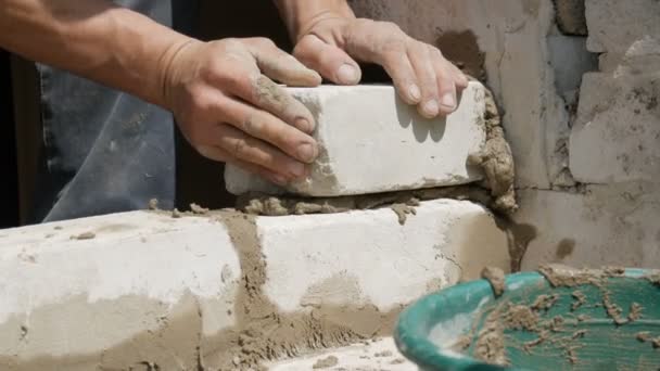 Las manos masculinas del constructor ponen el ladrillo sobre el cemento fresco mojado. Una fila de ladrillos blancos en un sitio de construcción vista de cerca. Pared — Vídeos de Stock