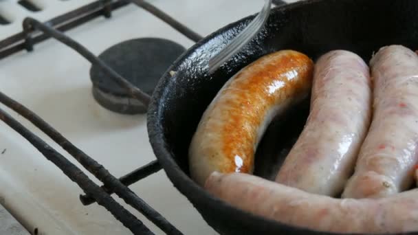Товсті жирні смачні свіжі ковбаски смажать на сковороді на домашній кухні. Смажені м'ясні продукти, що виготовляють сосиски для пива. Вилка перетворює смажені ковбаски — стокове відео