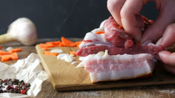Kvinnliga händer hugger med kniv och fyllda kryddor med skivor av vitlök och morötter en bit färskt rått kött fläskstek eller bacon i rustik stil på trä köksbord. — Stockvideo