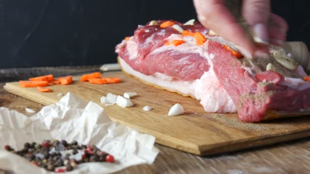 Las manos hembras apuñalan con un cuchillo y condimentos rellenos con rodajas de ajo y zanahorias un trozo de carne fresca cruda de cerdo o tocino en un estilo rústico en tablero de cocina de madera. — Vídeo de stock