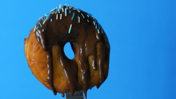Großer runder Donut auf einer Gabel, auf der Schokoglasur und blaues Puder auf blauem Hintergrund rotieren — Stockvideo