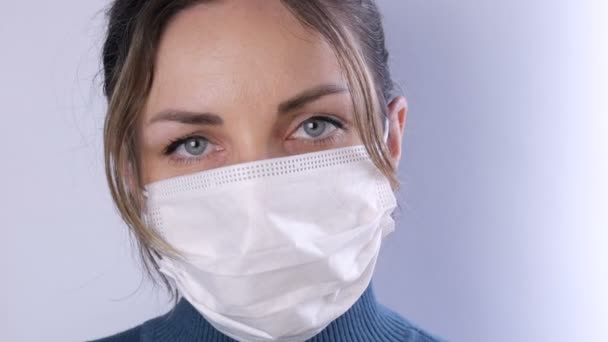 Πορτρέτο Όμορφη νεαρή γυναίκα με διαποτισμένα μαλλιά με κουρασμένα μάτια σε ιατρική μάσκα σε λευκό φόντο γκρο πλαν άποψη. Νοσοκόμες, ιατρικό προσωπικό κατά την επιδημία. Υγεία Coronavirus περίθαλψη και ιατρική έννοια — Αρχείο Βίντεο