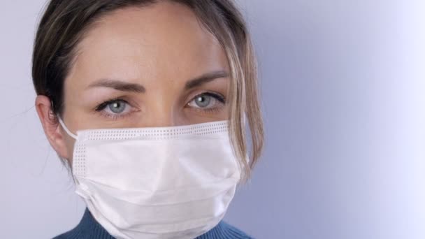 Retrato Hermosa mujer joven con el pelo alborotado con los ojos cansados en la máscara médica sobre un fondo blanco vista de cerca. Enfermeras, personal médico durante la epidemia. Salud Coronavirus y concepto médico — Vídeo de stock