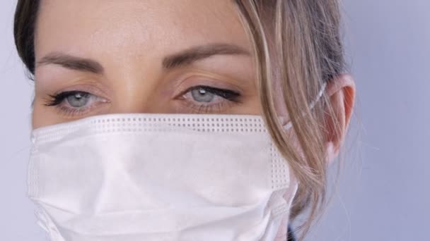 Портрет Красивая молодая женщина с взъерошенными волосами с уставшими глазами в медицинской маске на белом фоне крупным планом. Медсестры, медицинский персонал во время эпидемии. Коронавирус и медицинская концепция — стоковое видео