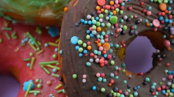 Американские пончики с красочной глазурью и порошком. Поворот на фиолетовом фоне закрыть вид — стоковое видео