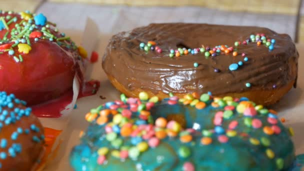 Large multi-colored fresh fried donuts in a row on a table. A beautiful donut with chocolate icing is sprinkled with a special colored powder for decoration of sweets — Stock Video