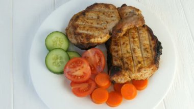 Lezzetli taze ızgara biftek ve domuz eti yanında vişneli domates ve taze sebzeli salatalık ve beyaz bir restoran tabağında döner.