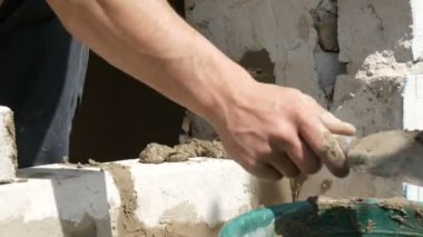Bir inşaatçının erkek eli taze ıslak çimentoya tuğla döşedi. İnşaat alanındaki bir sıra beyaz tuğla. Yakın görüş alanında. Duvar