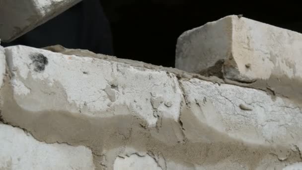 Las manos masculinas del constructor ponen el ladrillo sobre el cemento fresco mojado. Una fila de ladrillos blancos en un sitio de construcción vista de cerca. Pared — Vídeos de Stock